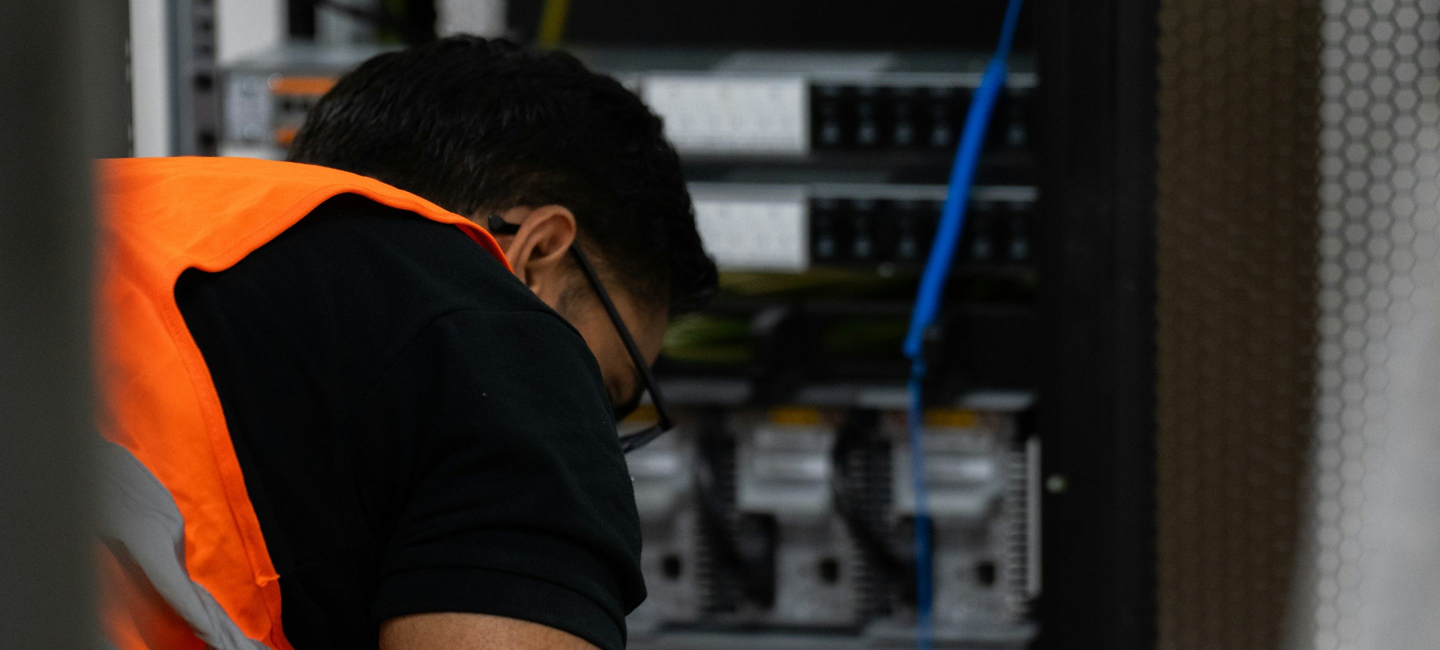 An engineer in a high-visibility vest working inside an equipment cabinet, with hand tools laid out beside them