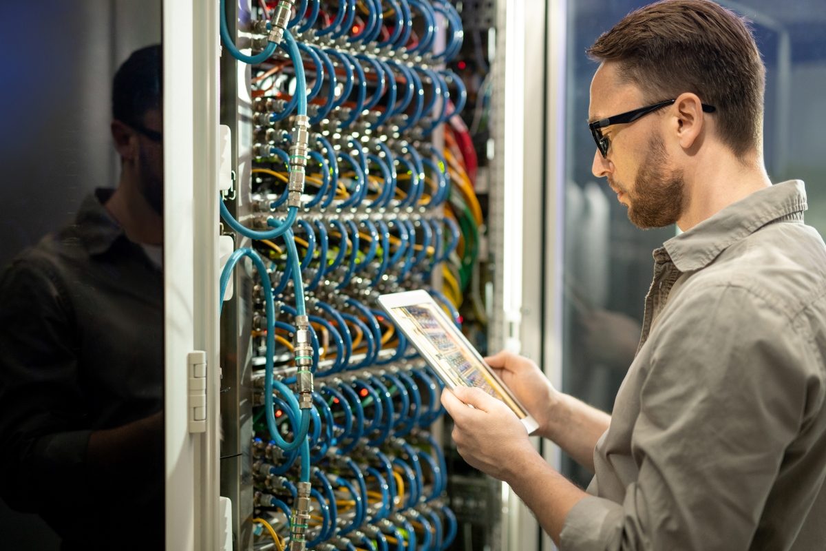 An engineer reading rack detail from a tablet in a data hall