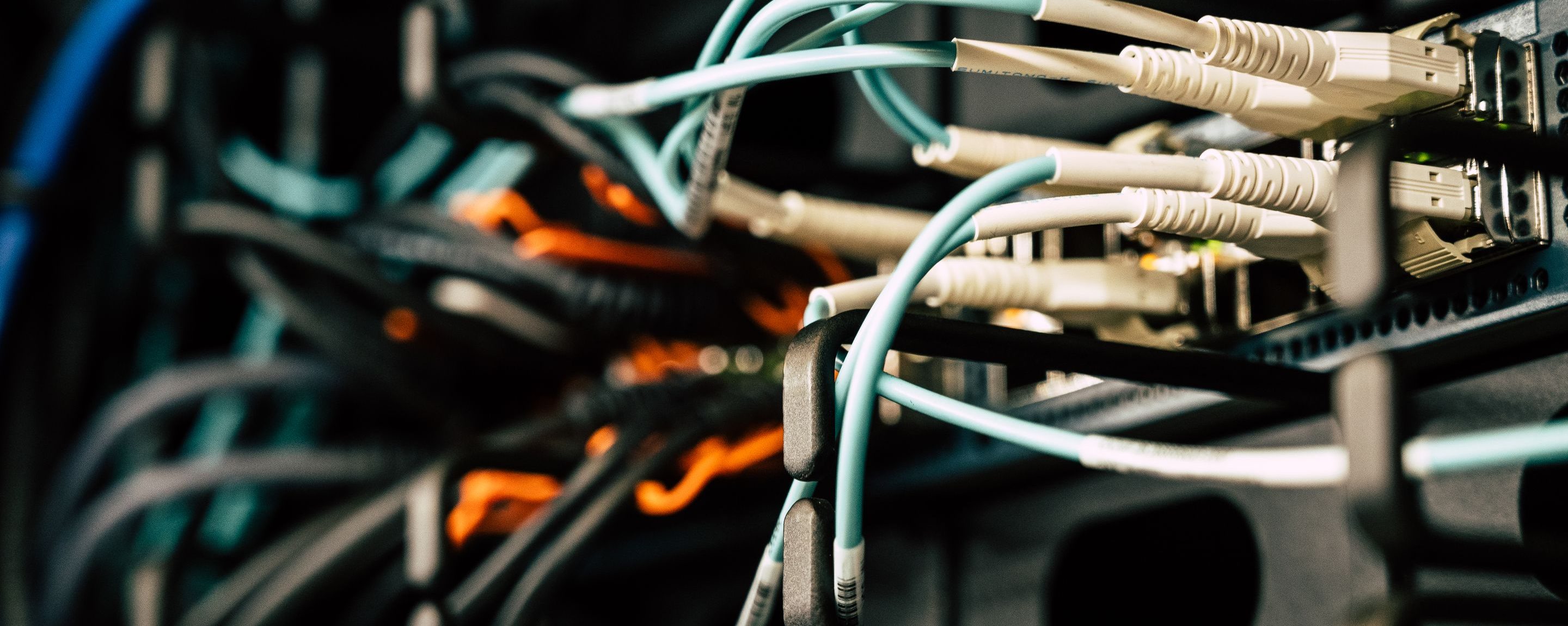 Teal and black patch cords running behind equipment in a cabinet, several bundles deep