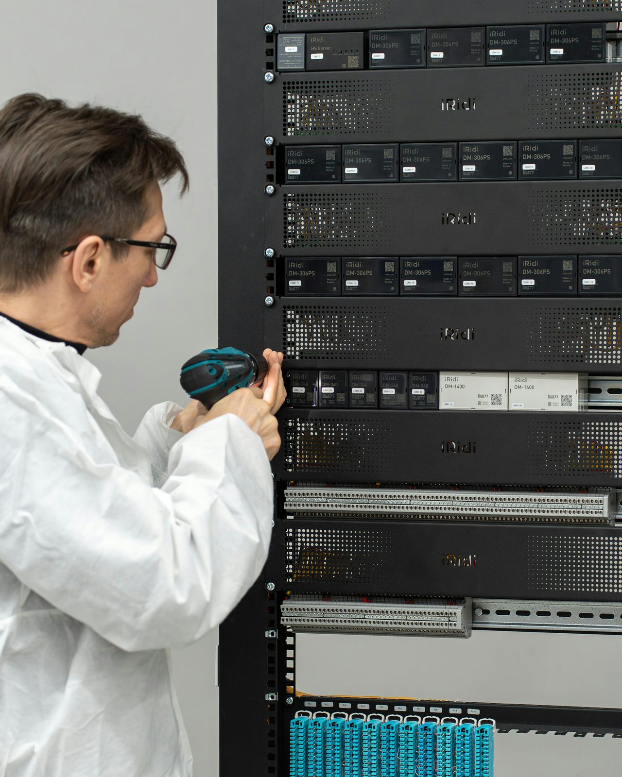 An engineer in a lab coat working at an open equipment rack of labelled modules, driver in hand