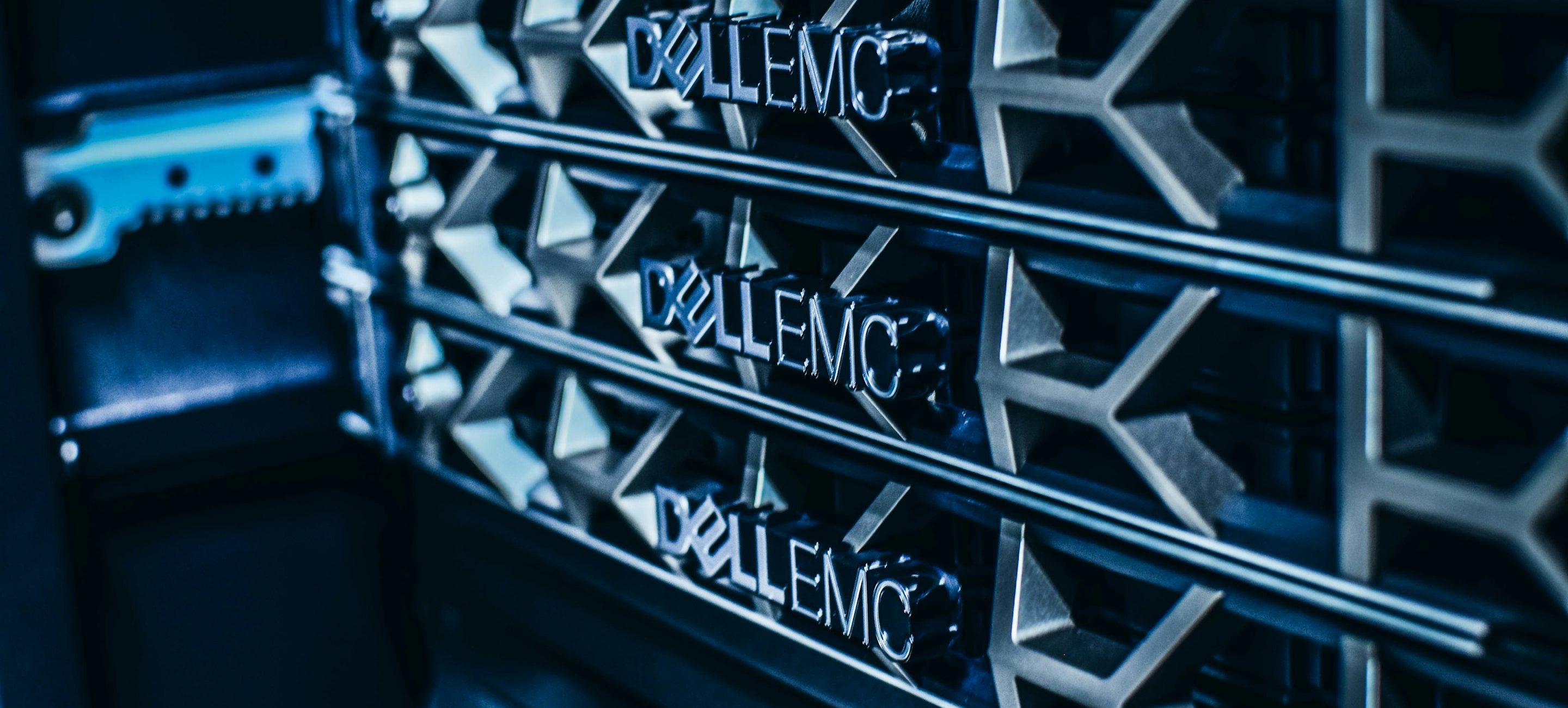 Manufacturer nameplates on the bezels of three rack-mounted storage chassis under low blue light