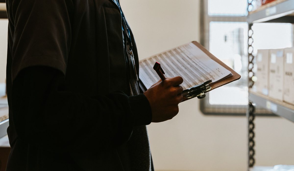 An auditor working through a checklist on a clipboard beside stored equipment