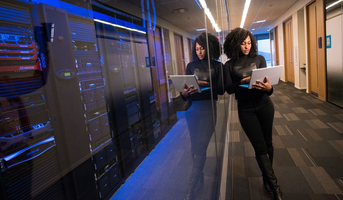 An engineer walking a data hall aisle with a laptop open