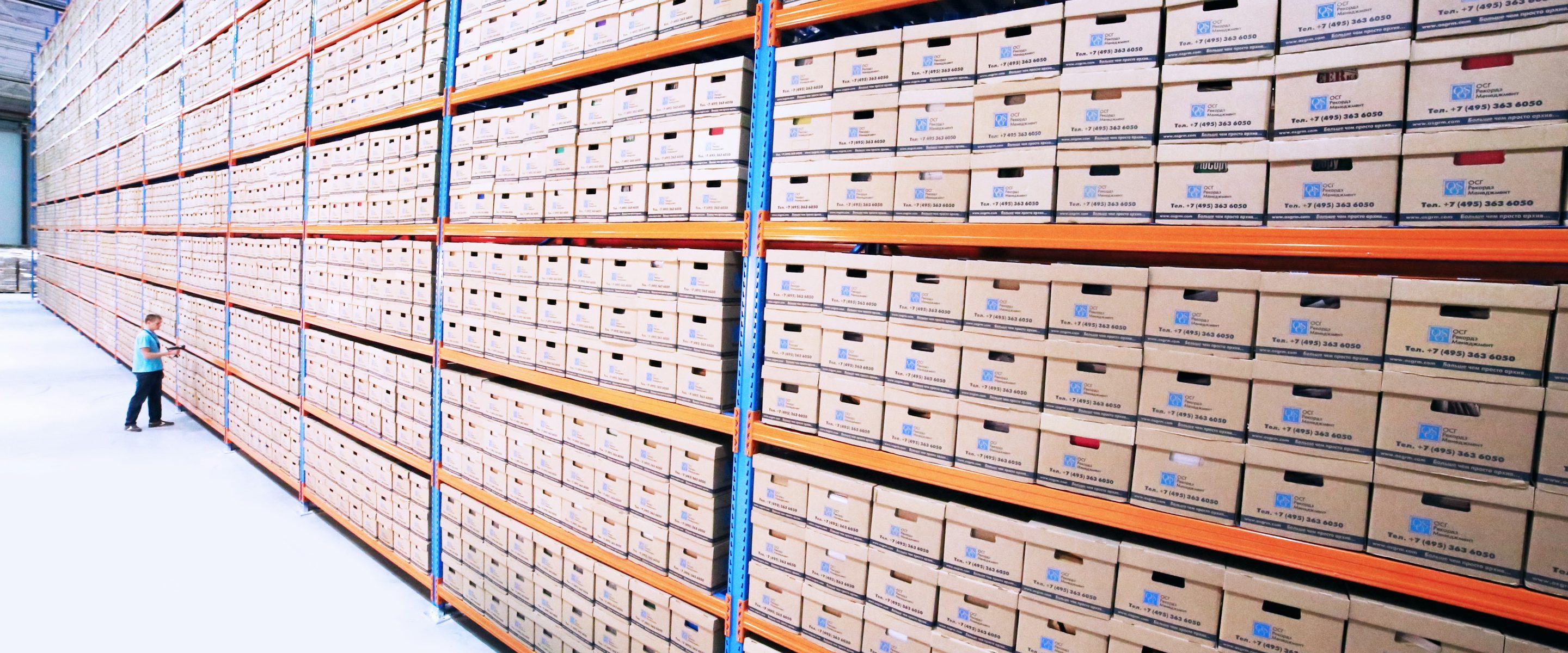 A records warehouse: a wall of archive boxes on racking, with a single person walking the aisle