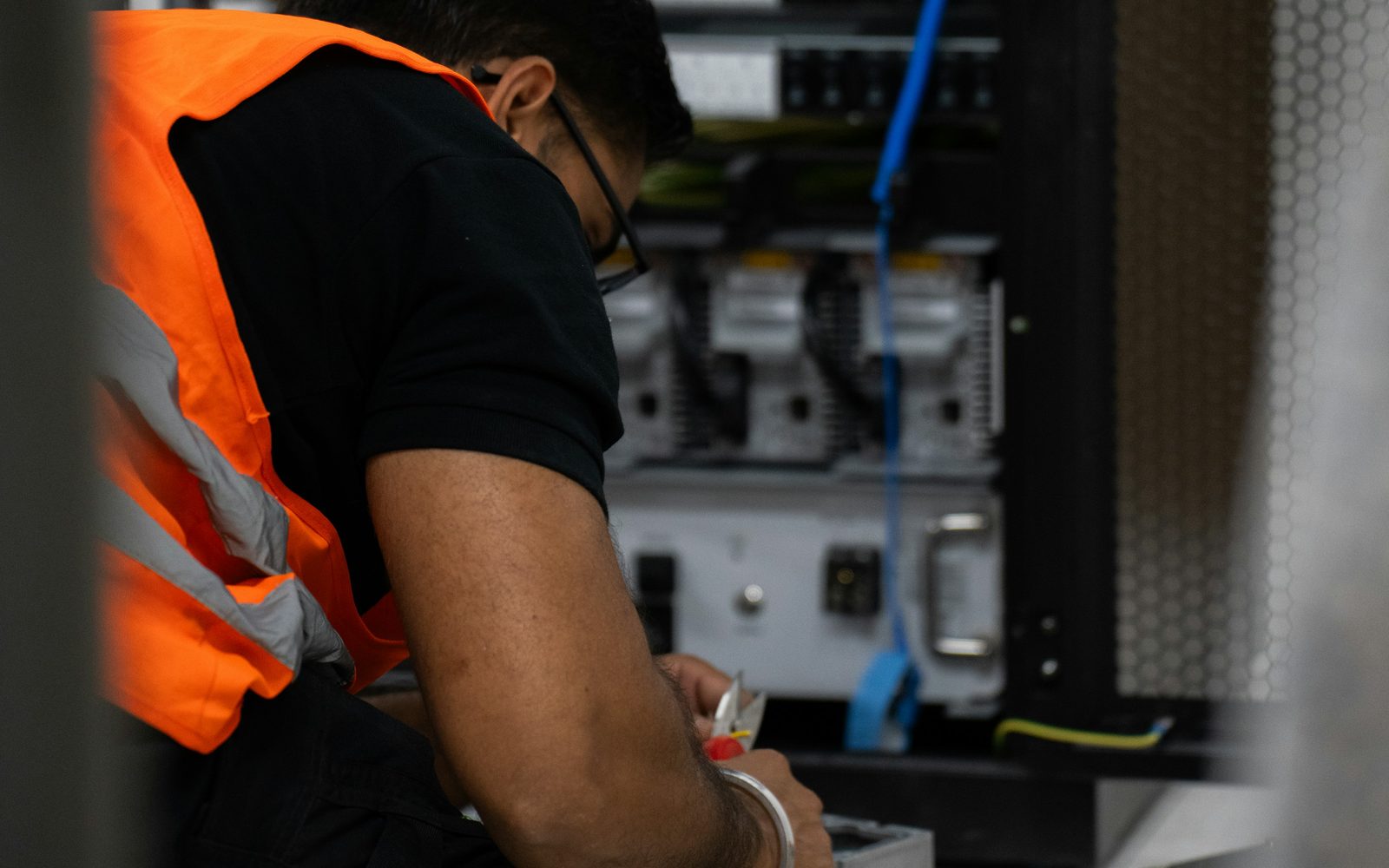 A technician in a high-visibility vest working inside an open equipment cabinet