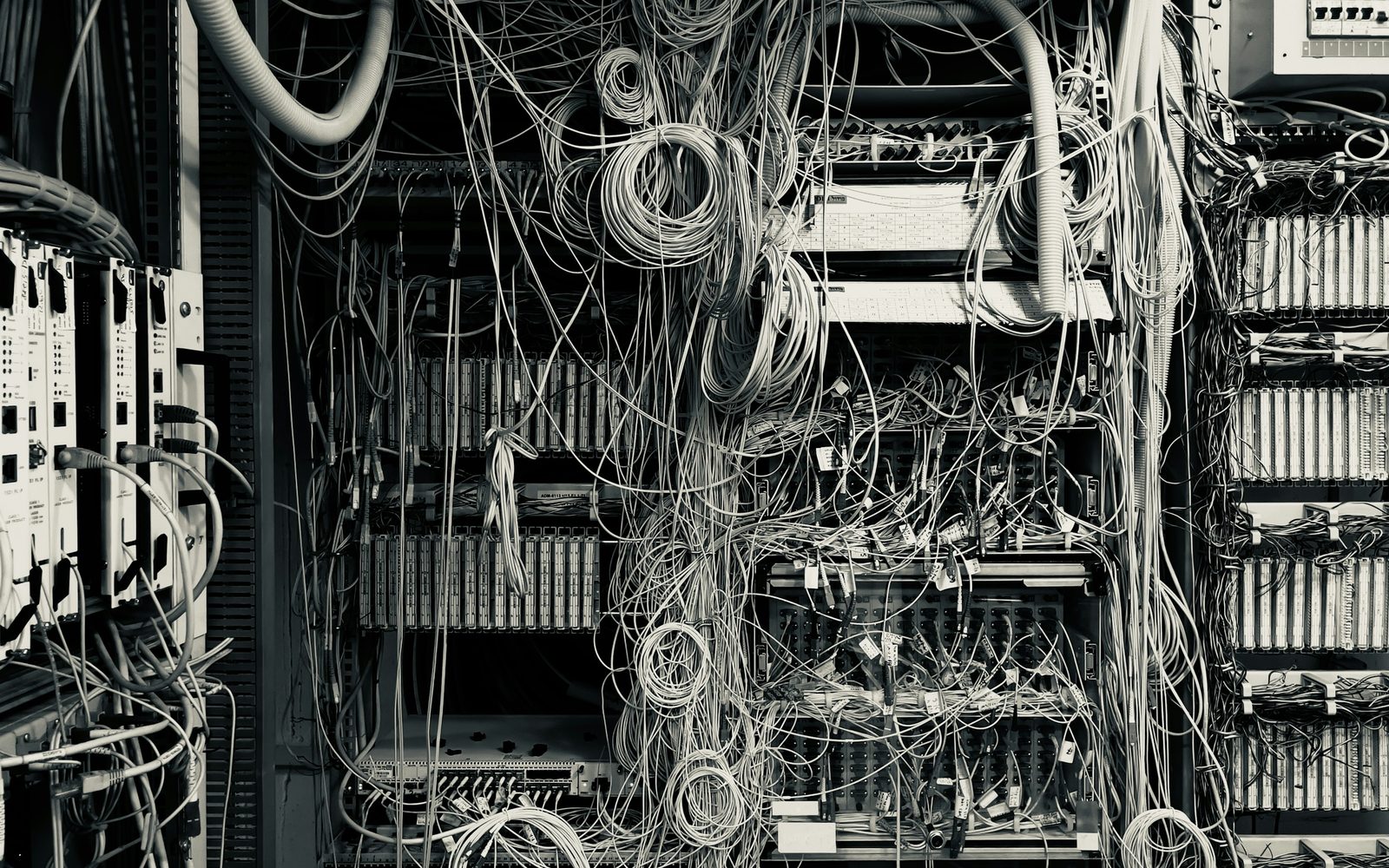 A dense legacy wiring frame photographed in black and white, cabling looped and layered across the racks
