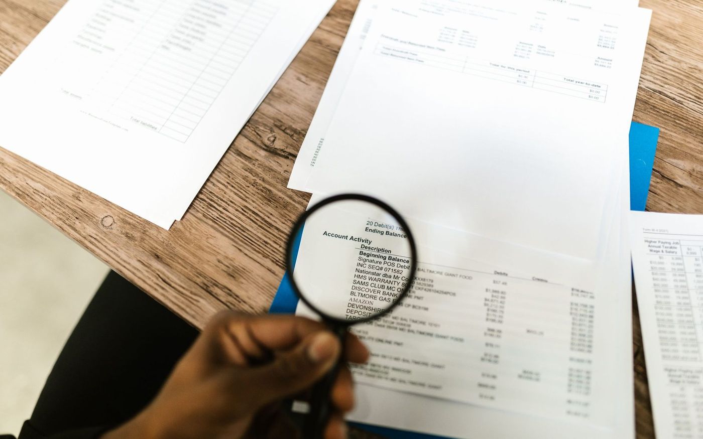Printed statements spread across a desk, one read through a magnifying glass