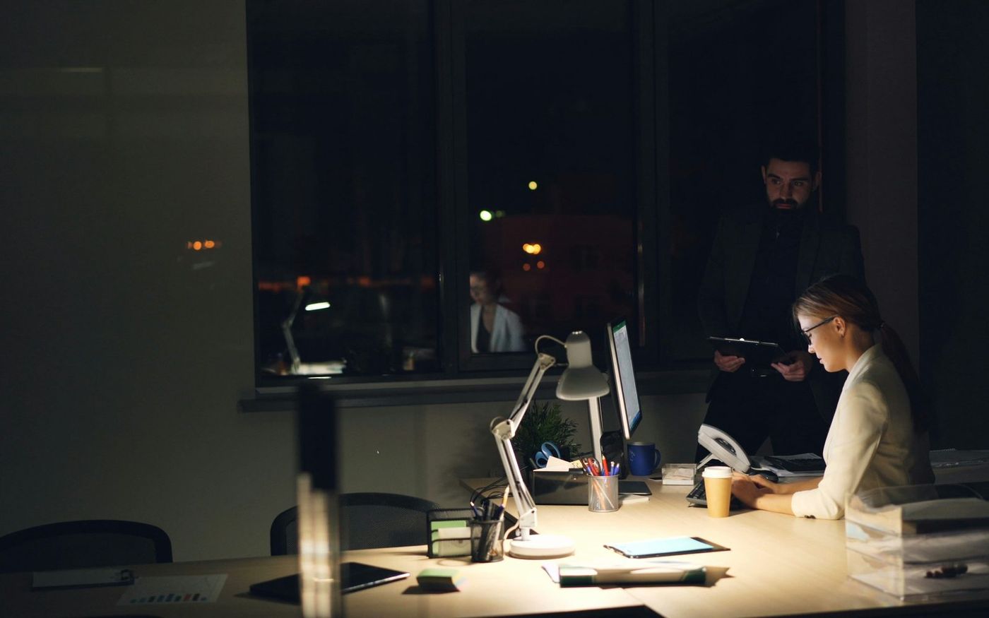 An on-call responder working late at a desk while a colleague looks on